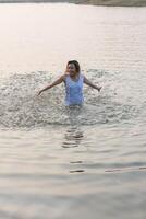 gelukkige mooie vrouw die een witte jurk draagt, geniet van het spelen van water in het meer. foto