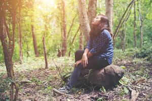 jonge hipster-vrouw probeerde te wandelen in het bos, rust uit op de rots terwijl ze wegkijkt naar de natuur. foto