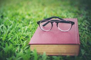 bril met rood boek op het groene gras in het park foto