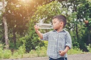 kleine schattige Aziatische jongen drinkt water langs de weg. foto