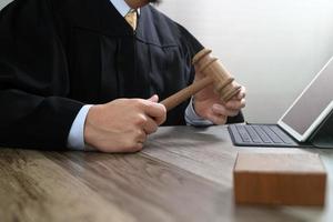 rechtvaardigheid en recht concept.male rechter in een rechtszaal met de hamer, werken met digitale tabletcomputer docking toetsenbord op houten tafel foto