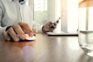 designer hand werken en slimme telefoon en laptop op houten bureau op kantoor foto