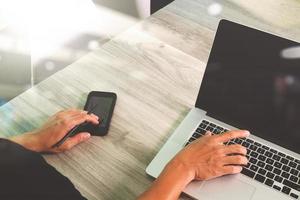 designer hand werken en slimme telefoon en leeg scherm laptop en digitale tablet op houten bureau op kantoor foto