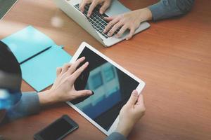 bovenaanzicht van twee collega's die gegevens bespreken met een leeg scherm nieuwe moderne computerlaptop en pro digitale tablet op houten bureau als concept foto