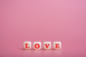 tekst houten blokken die het woord liefde spellen op roze achtergrond foto