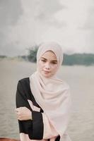 mooi islamitisch vrouwelijk model met hijab-mode, een moderne trouwjurk voor moslimvrouwen die in het zand en op het strand zitten. portret van een Aziatisch meisjesmodel dat hijab gebruikt en plezier heeft op het strand met bomen foto