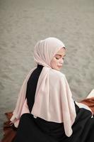 mooi islamitisch vrouwelijk model met hijab-mode, een moderne trouwjurk voor moslimvrouwen die in het zand en op het strand zitten. portret van een Aziatisch meisjesmodel dat hijab gebruikt en plezier heeft op het strand met bomen foto