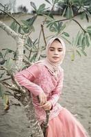 mooi islamitisch vrouwelijk model met hijab-mode, een moderne trouwjurk voor moslimvrouwen die in het zand en op het strand zitten. portret van een Aziatisch meisjesmodel dat hijab gebruikt en plezier heeft op het strand met bomen foto