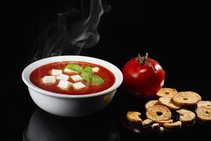 tomatensoep. huisgemaakte tomatensoep met stukjes mozzarella, tomaten, kruiden, specerijen en verse basilicum. met geroosterde bruschetta's ernaast. foto