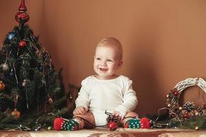 mooie kleine babyjongen die kerst viert. grappig kind in een kerstpak bij de kerstboom in de kamer foto