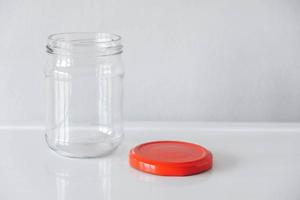 lege glazen pot met rode deksel op witte tafel achtergrond foto