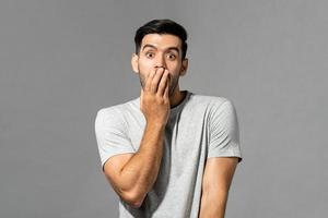 portret van een geschokte jonge blanke man met de hand die de mond bedekt op een lichtgrijze studioachtergrond foto