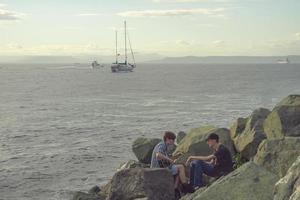 vladivostok, primorsky krai-26 augustus 2018 - jonge mannen die gitaar spelen aan zee op de achtergrond van schepen op. foto