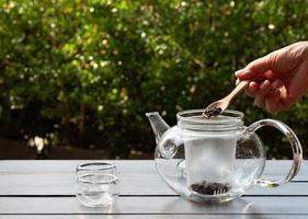 vrouw die theeblaadjes toevoegt aan theepot om hete thee te maken foto