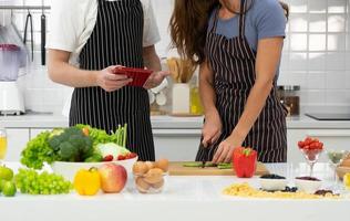 jonge vrouw die groente hakt terwijl haar man instructies leest over het koken van een gezonde salade voor het ontbijt in de keuken. koppel samen concept foto