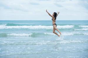 schoonheidsvrouwen die met bruine zwempakbikini op een strand en golfzee springen foto