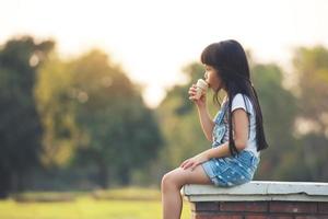 kleine kinderen meisje zitten eten met ijs op grren park achtergrond foto