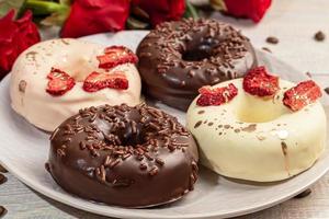 handgemaakte donuts op een lichte achtergrond in witte en zwarte chocolade. er zijn bloemen in de buurt. vrouwendag, valentijnsdag. foto