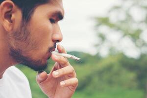 jonge hipster man die rust neemt, een sigaret rookt met de natuur en een frisse bries. foto