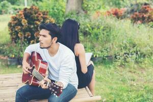 jonge charmante paar verliefd akoestische gitaar spelen in het park.relaxing met natuur, lifestyle concept. foto