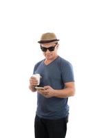 jonge hipster man kijken naar zijn slimme telefoon en koffie in handen geïsoleerd op een witte achtergrond. foto