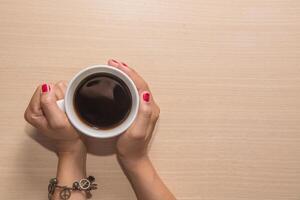 vrouw handen houden een kopje koffie op houten tafel. foto