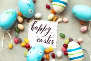 gelukkig Pasen-concept. voorbereiding op vakantie. paaseieren inscriptie happy easter letters candy chocolade-eieren en jellybean snoepjes op betonnen steen grijze achtergrond. plat lag bovenaanzicht kopieerruimte. foto