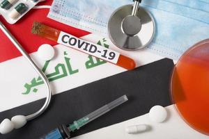 coronavirus, het concept covid-19. bovenaanzicht van een beschermend ademhalingsmasker, stethoscoop, spuit, pillen op de vlag van irak. foto