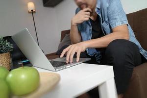 hipster hand met behulp van laptop compter betalingen online zaken, zittend op de bank in de woonkamer, groene appels in houten dienblad, thuiswerk concept, foto