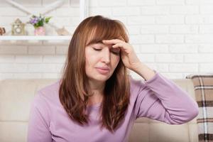 brunette vrouw van middelbare leeftijd met hoofdpijn op de achtergrond van het huis. menopauze foto