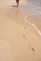 blanke vrouw gezien vanaf haar rug lopen op een leeg strand. Voetafdrukken in het zand. bloedsomloop wordt verbeterd door aërobe oefening, zoals wandelen aan de kust. Portugal foto