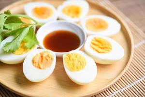 eieren ontbijt, verse eieren menu eten gekookte eieren in een houten bord versierd met bladeren, groene selderij en vissaus op houten ondergrond, in tweeën gesneden eierdooiers voor het koken van gezond eten foto