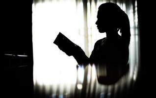silhouet jonge vrouw die een boek leest in de woonkamer foto