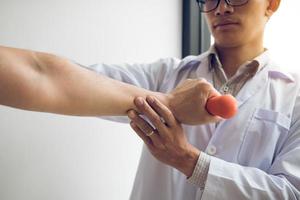 Aziatische fysiotherapeut die een patiënt helpt die dumbbells optilt om zijn herstel te doorlopen met gewichten in de kliniekkamer. foto