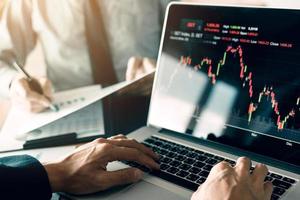 investeerders gebruiken laptops om de aandelenmarkt van investeringswebsites te betreden en partners maken aantekeningen en analyseren prestatiegegevens.