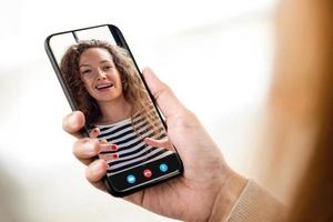 jonge lachende blanke vrouw met videogesprek met vriend op mobiele telefoon foto