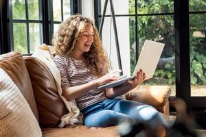 Gelukkig lachende blanke vrouw chatten via video-oproep met laptopcomputer op de bank in de woonkamer thuis overdag foto