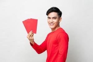 Glimlachende knappe Aziatische man met rode enveloppen of ang pow in studio geïsoleerde grijze achtergrond voor Chinees Nieuwjaar concepten foto