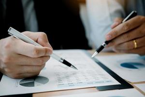 twee zakenlieden die een pen vasthouden die naar de kostengrafiek van het bedrijf wijst en samen financiële analyses maken. foto