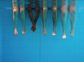 benen van Afro-Amerikaanse man met blanke vrienden in zwembad onder water. zomer. vakantie, internationaal en sportconcept. foto