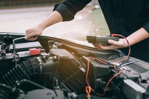 automonteur controleert de motor en houdt de batterijmeter vast. foto