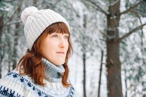 winterportret van een vrouw in een warme muts en trui op een achtergrond van besneeuwd bos foto