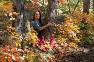 lachende vrouw met rode indische broek zittend in het bos onder de bomen op het pad met herfstgebladerte. portret van een gelukkige vrouw foto