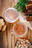 twee glazen light bier en snacks, pistachenoten en croutons op een houten tafel foto