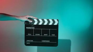 de hand houdt een lege filmklapper vast op een gekleurde achtergrond in de studio foto