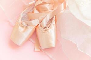 nieuwe pastel beige balletschoenen met satijnen lint en tutut rok geïsoleerd op roze achtergrond. ballerina klassieke spitzen voor danstraining. balletschoolconcept. bovenaanzicht plat leggen, ruimte kopiëren foto