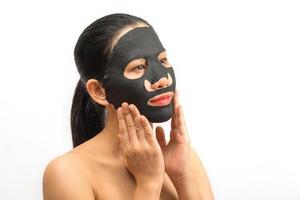 jonge vrouw die een zwart gezichtsmaskerblad doet met een zuiverend masker op haar gezicht op een witte achtergrond foto