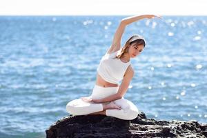 jonge vrouw die yoga doet op het strand met witte kleren aan foto