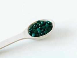 groene hawaiiaanse spirulina in eetlepels pillen in houten lepel op groene achtergrond. superfood, gezonde levensstijl, gezonde supplementen, superfoods in kookconcept foto