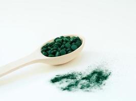 groene hawaiiaanse spirulina in eetlepels pillen in houten lepel op groene achtergrond. superfood, gezonde levensstijl, gezonde supplementen, superfoods in kookconcept foto